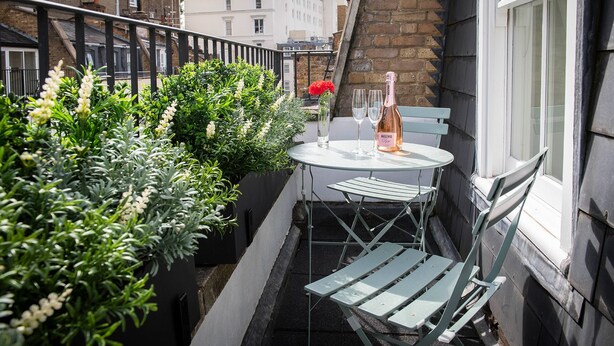 Un petit espace extérieur aménagé avec une table et des chaises, une bouteille de vin et des plantes en pot.