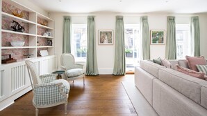 Un salon comprenant un fauteuil à motifs à carreaux, un canapé et une étagère blanche agrémentée d’objets décoratifs.