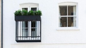 Une maison de ville blanche avec une porte vert foncé, un banc en bois et deux fenêtres dot ées de balustrades noires.