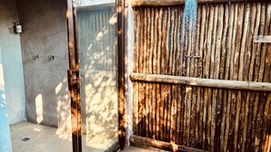 A glass door leading to a concrete patio area with a wooden fence and a hanging showerhead. - Leadwood Tree Safari Lodge  (Hoedspruit)