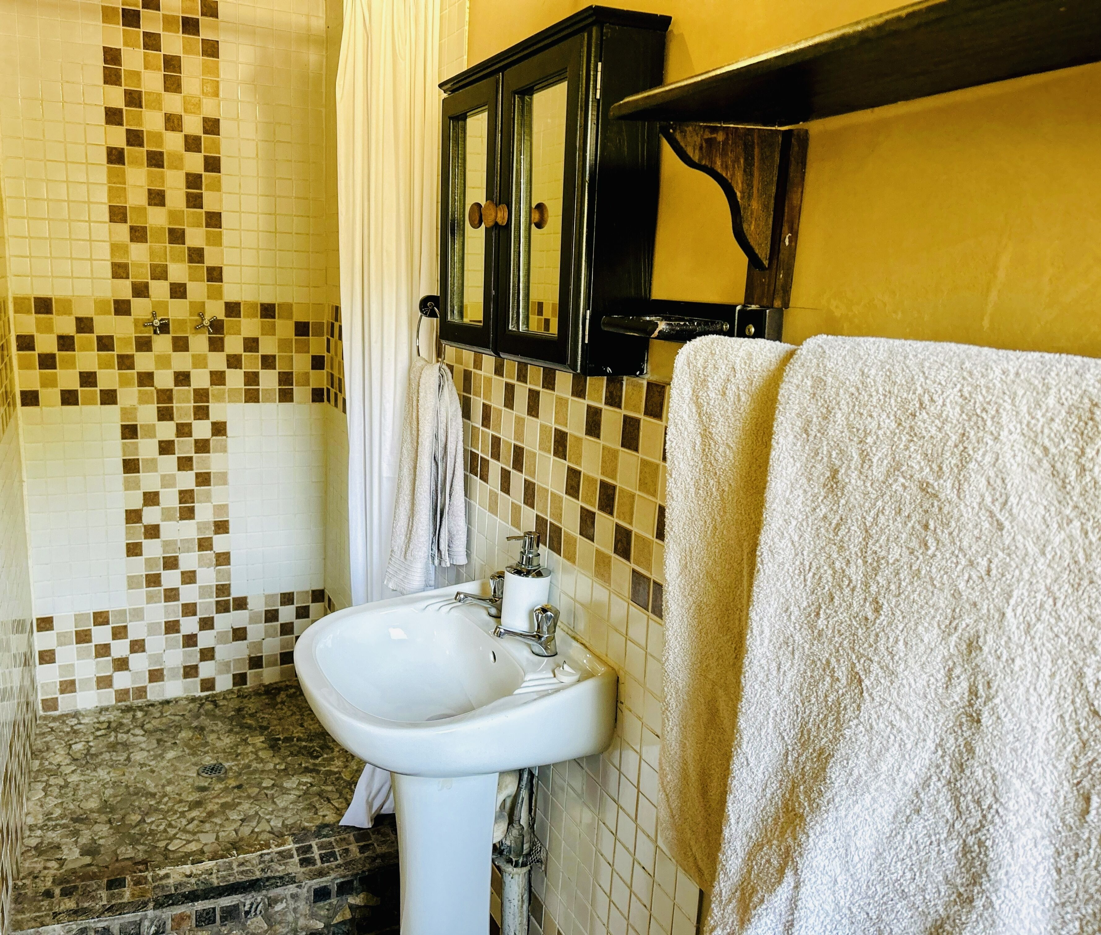 A bathroom with a tiled floor, a white sink, a mirror, and a towel hanging on the wall.