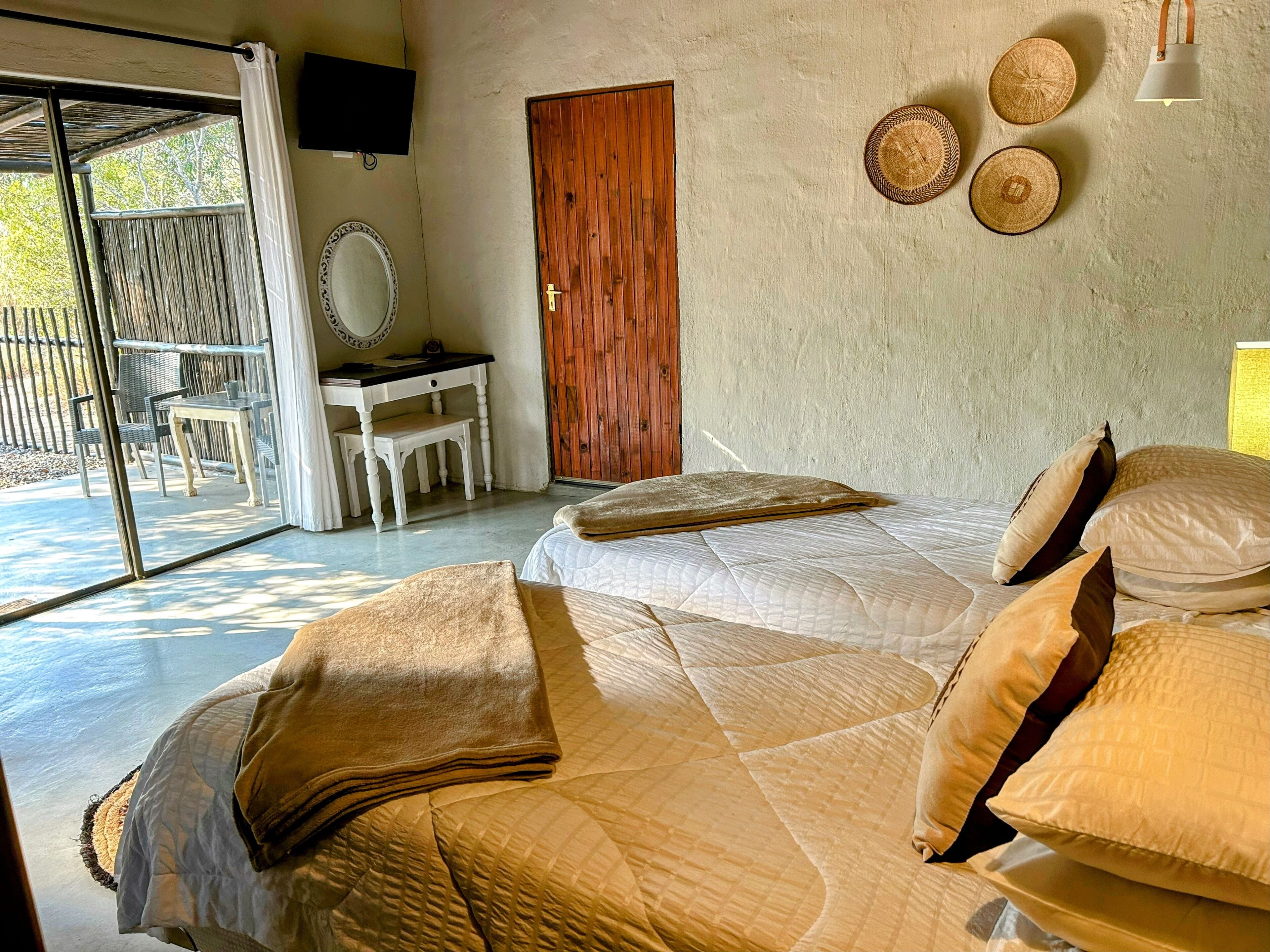 Une chambre avec deux lits, une porte en bois, un bureau avec une chaise et une grande fenêtre.
