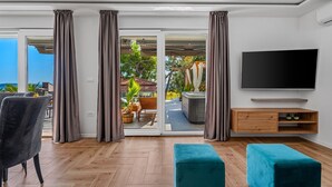 A modern living room with a large TV, wooden flooring, and a sliding glass door leading to an outdoor area with a hot tub and patio furniture. - Villa Lea with 4 bedrooms, 40sqm pool, Hot-Tub, 2km from the beach (Kastel Novi)