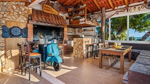 A rustic outdoor dining area with a stone wall, wooden furniture, and a blue scooter. - Villa Lea with 4 bedrooms, 40sqm pool, Hot-Tub, 2km from the beach (Kastel Novi)