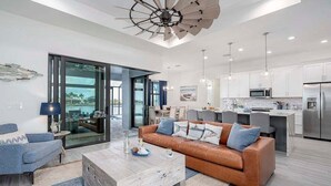 A modern living room with a leather sofa, a coffee table, and a dining area with a kitchen in the background. - Castaway Cape - Luxury Rental with Outdoor Kitchen (Cape Coral)