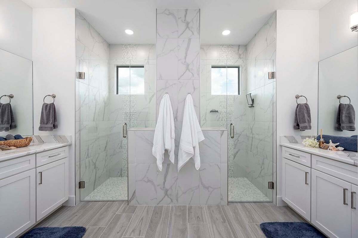 A modern bathroom with a glass-enclosed shower, marble walls, and white cabinets.