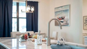 A modern kitchen with a central island, a built-in sink, and a dining area with a chair. - Castaway Cape - Luxury Rental with Outdoor Kitchen (Cape Coral)