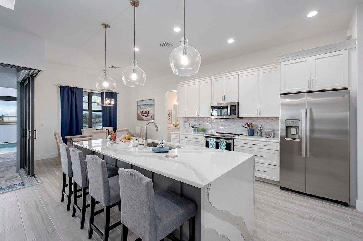 A modern kitchen with a large island, stainless steel appliances, and pendant lighting.