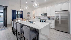 A modern kitchen with a large island, stainless steel appliances, and pendant lighting. - Castaway Cape - Luxury Rental with Outdoor Kitchen (Cape Coral)