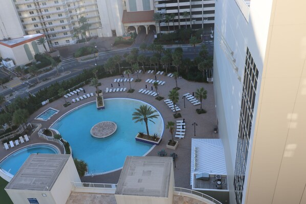Zona de piscina en la azotea con sillones de descanso y palmeras, rodeada de edificios.