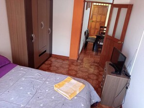 Un dormitorio con cama, armario, escritorio con computadora y televisor.