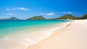 A beach with clear turquoise water, a sandy shore, and green hills in the background.
