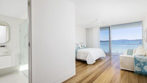 A modern hotel room with a large bed, a sofa, and a view of the sea. - Whitehouse On The Water - Palatial Home on Idyllic Beach (Corlette)