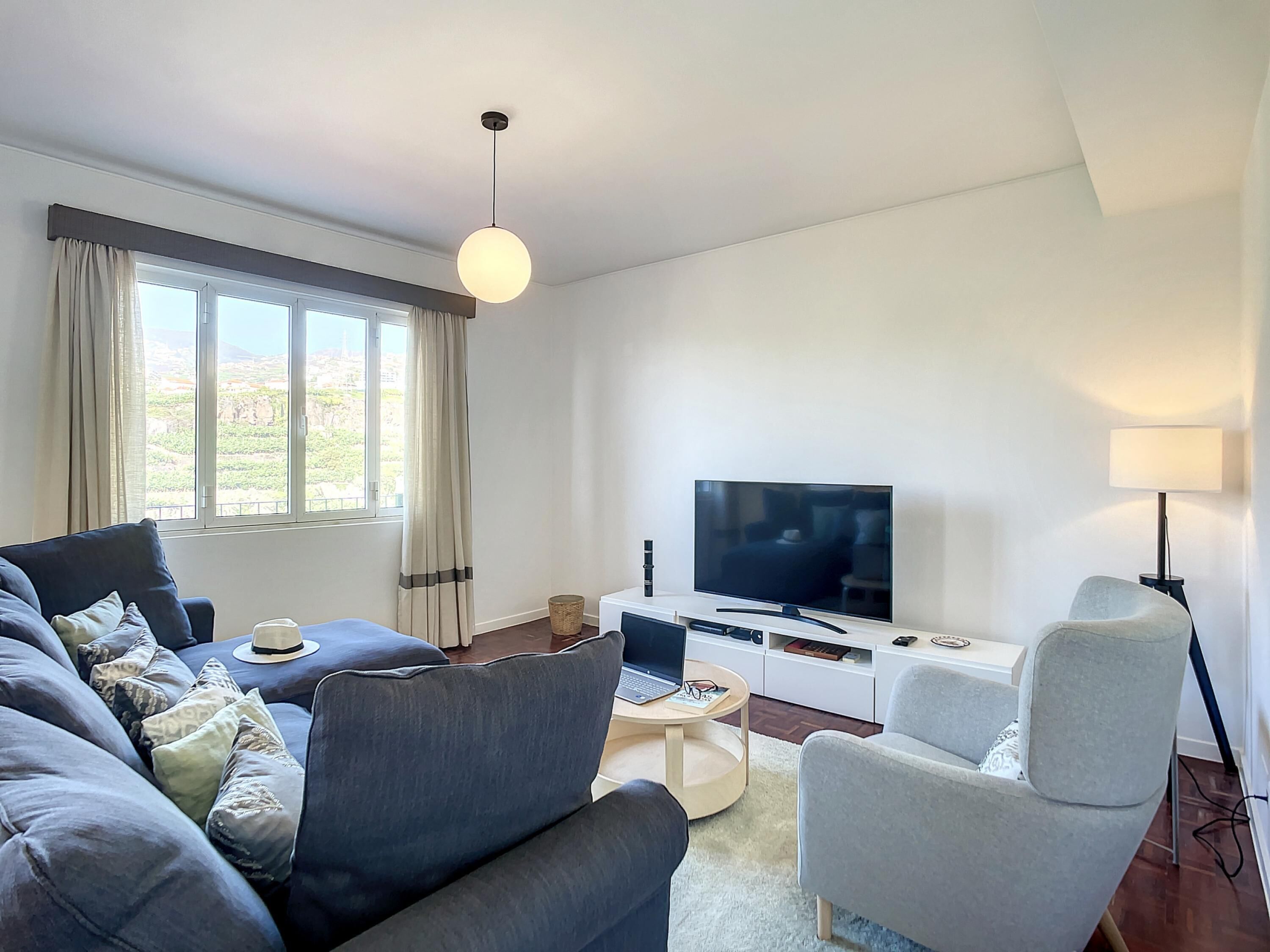 Un salon moderne avec un canapé, des fauteuils, un téléviseur et une lampe.