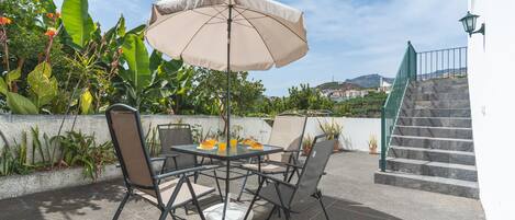 Un patio al aire libre con una mesa, sillas, un paraguas y vista a un paisaje urbano de fondo.