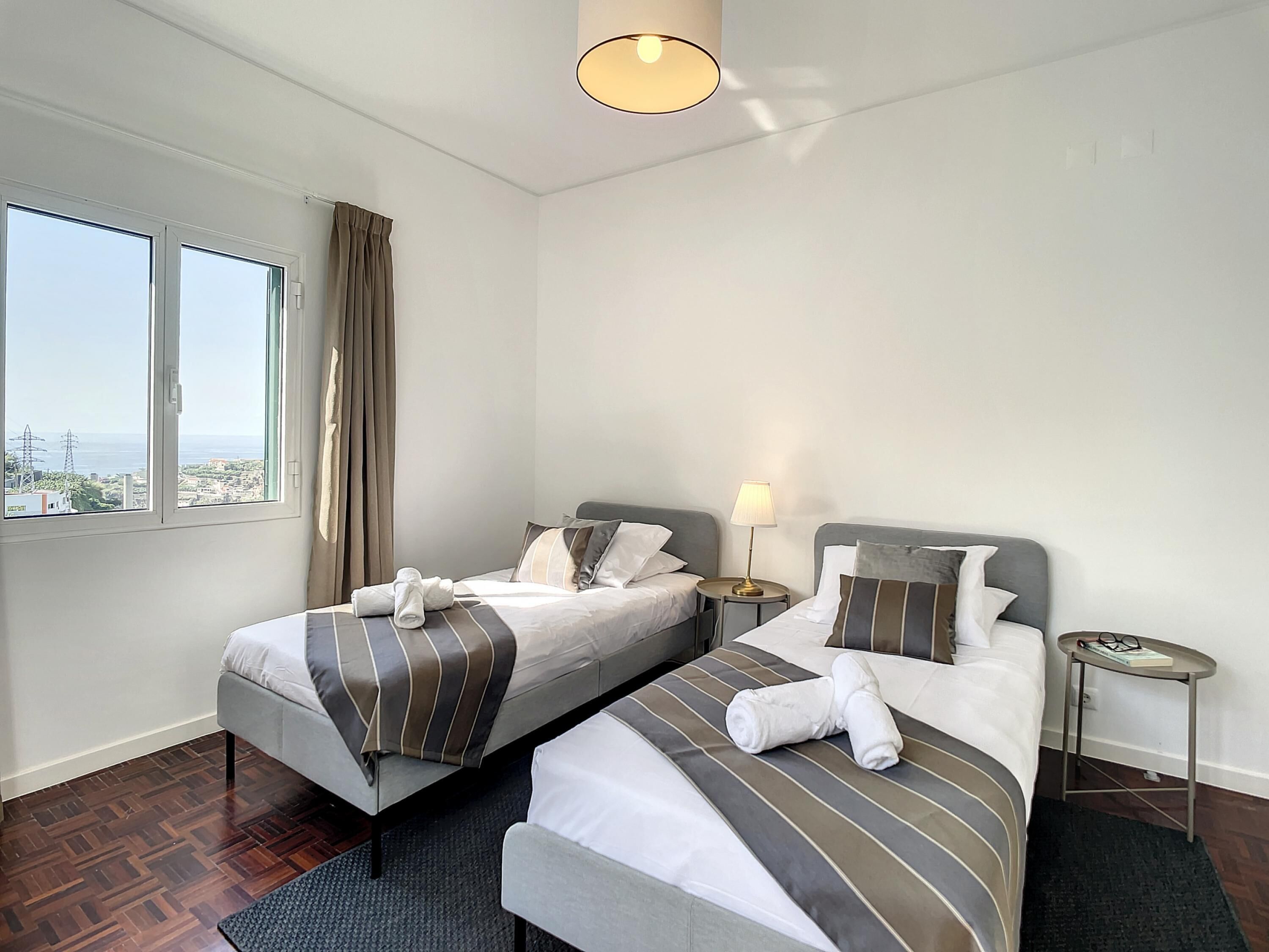 Une chambre d’hôtel avec deux lits, une vue sur la ville et une petite table avec une lampe.