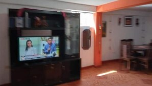 Un salon équipé d’un téléviseur à écran plat posé sur un meuble, d’un réfrigérateur et d’un coin repas avec une table et des chaises.