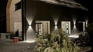 Ein modernes Gebäude mit geneigtem Dach, großen Fenstern und einem gut beleuchteten Eingang.