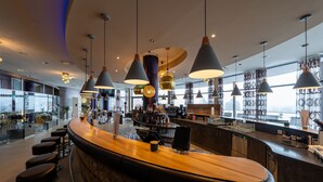 A modern bar area with a curved counter, multiple pendant lights, and a view of the city through large windows. - Hotel AVIVA make friends - Singles only (Sankt Stefan-Afiesl)