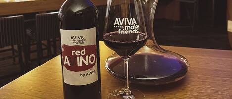 A bottle of red wine and a glass with "AVIVA makes friends" on a wooden table in a bar setting.