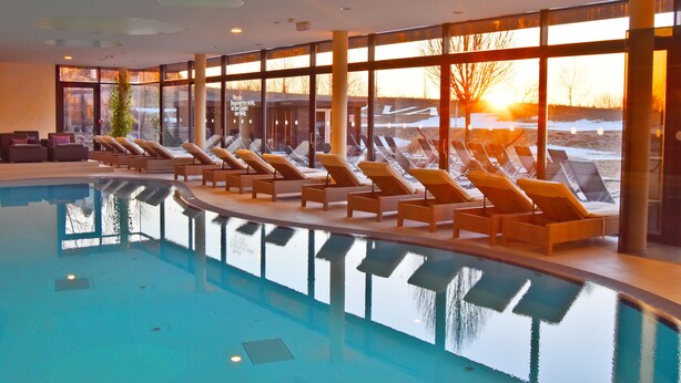 An indoor swimming pool with lounge chairs and large windows offering a view of the sunset. - Hotel AVIVA make friends - Singles only (Sankt Stefan-Afiesl)