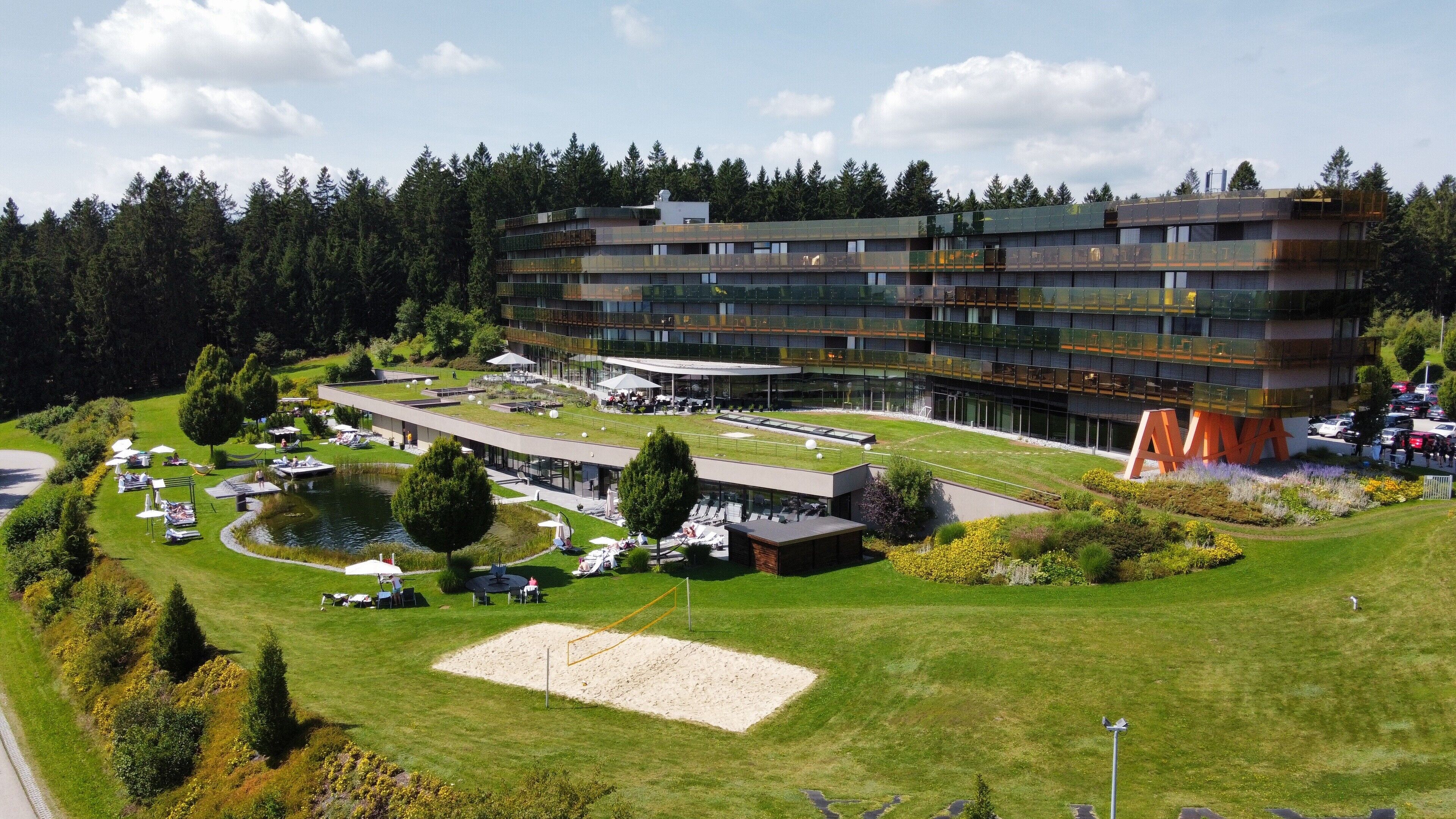 A modern hotel with a rooftop terrace, a swimming pool, and a well-maintained garden.