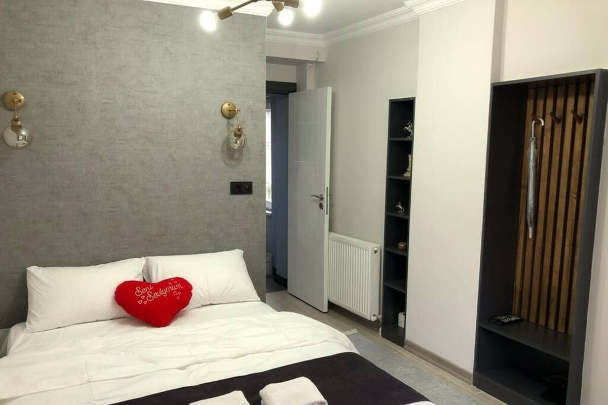 A bedroom with a bed, a red heart-shaped pillow, two folded towels, a wardrobe, and a radiator.