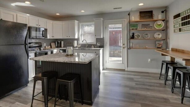 Una cocina moderna con armarios blancos, un refrigerador negro, electrodomésticos de acero inoxidable y una isla central con taburetes.