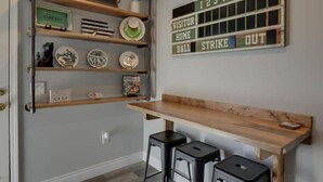 Una cocina con encimera de madera, dos taburetes negros y un estante en la pared con platos y un marcador de puntos.