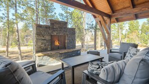 An outdoor patio with a stone fireplace, wicker furniture, and a view of the surrounding forest. - Incredible Craftsman Style Spacious Lodge Walking Distance to Clubhouse! (Lead)