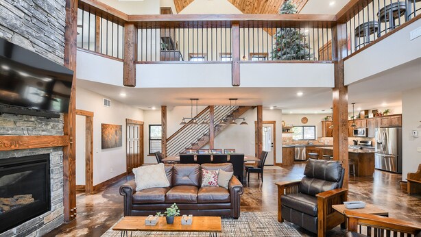 A spacious living area with a fireplace, leather sofa, and a dining area with a staircase leading to a balcony. - Incredible Craftsman Style Spacious Lodge Walking Distance to Clubhouse! (Lead)