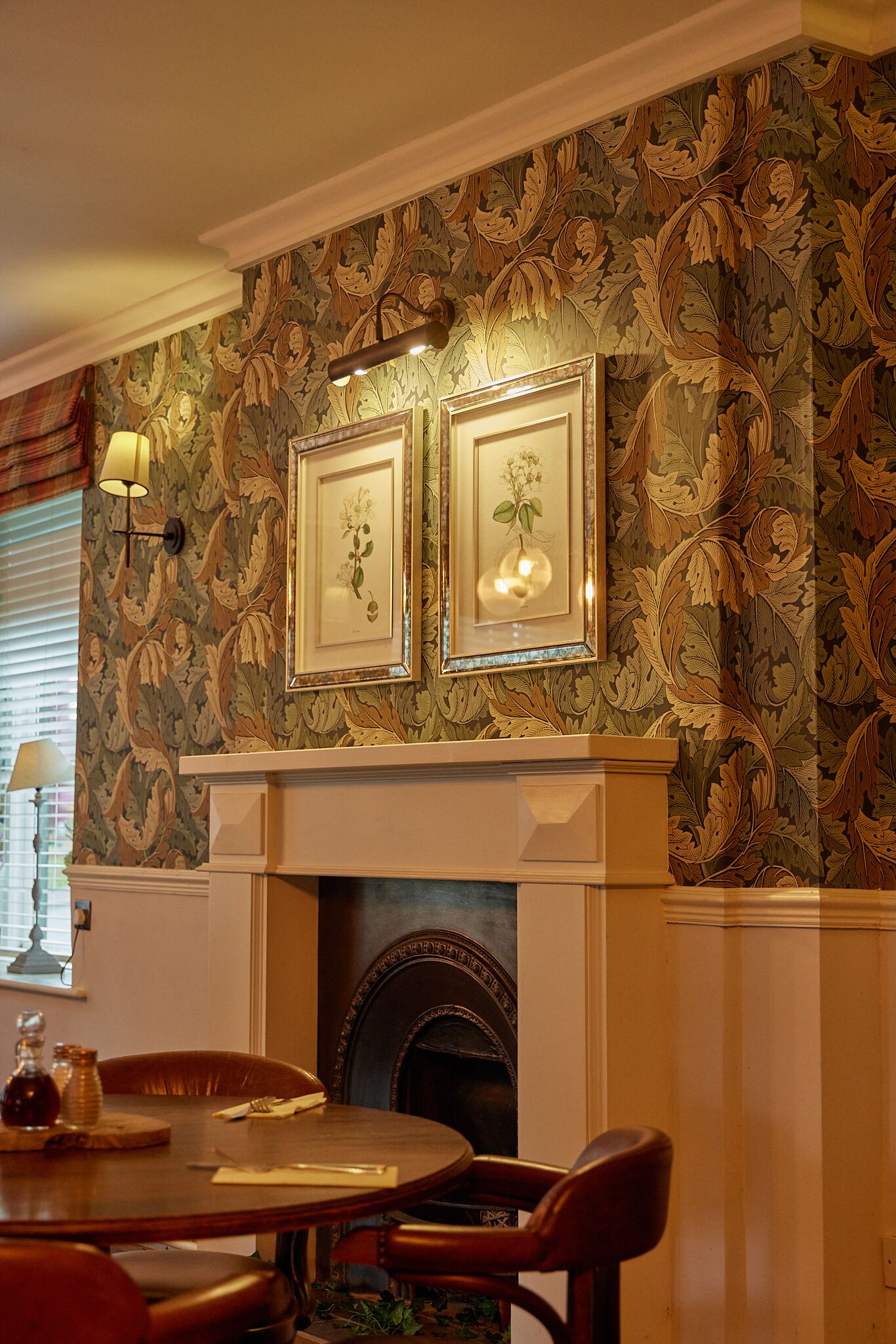 A dining area with a fireplace, a table, chairs, and framed artwork on the wall.