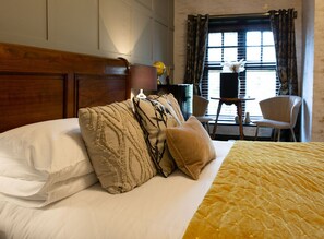 A neatly made bed with white and patterned pillows, a yellow quilt, and a wooden headboard.
