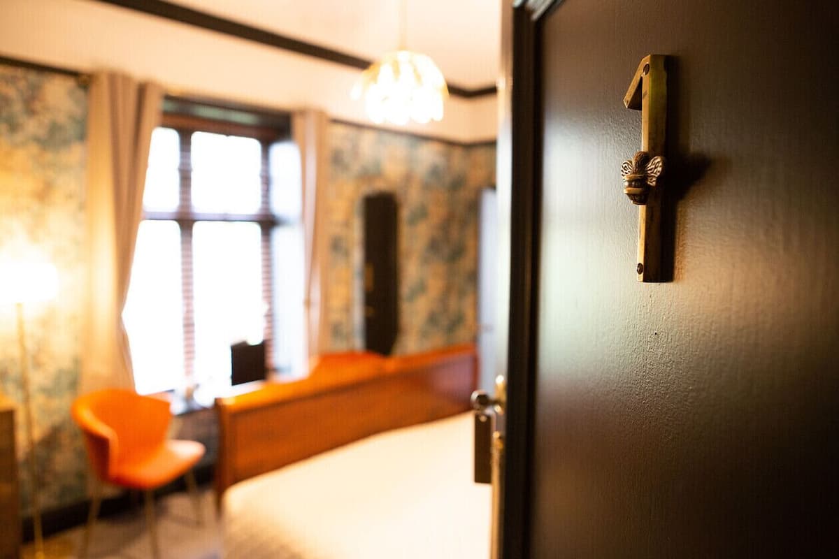 Quarto de hotel com cama, uma cadeira, janela e porta.