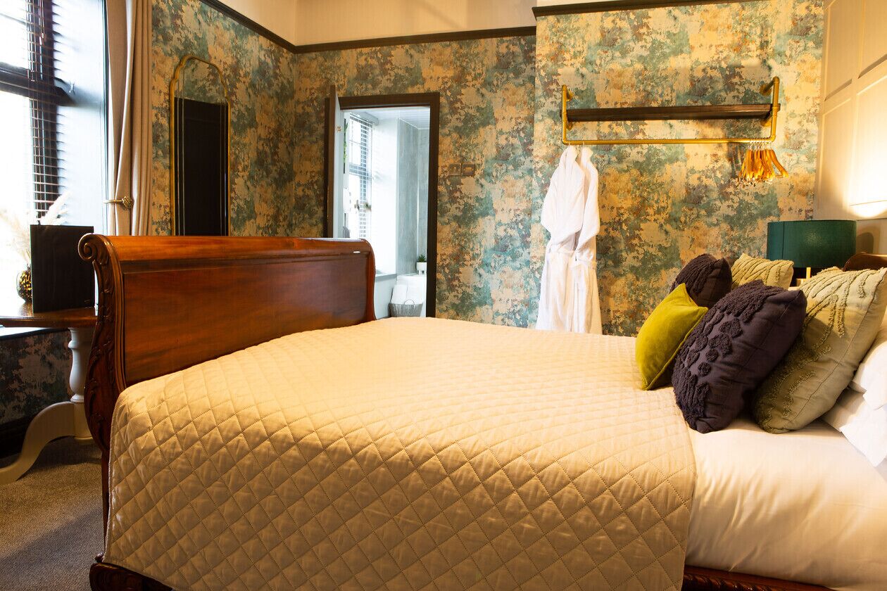 Een slaapkamer met een groot bed, een houten hoofdbord, een spiegel en een rustieke wand.