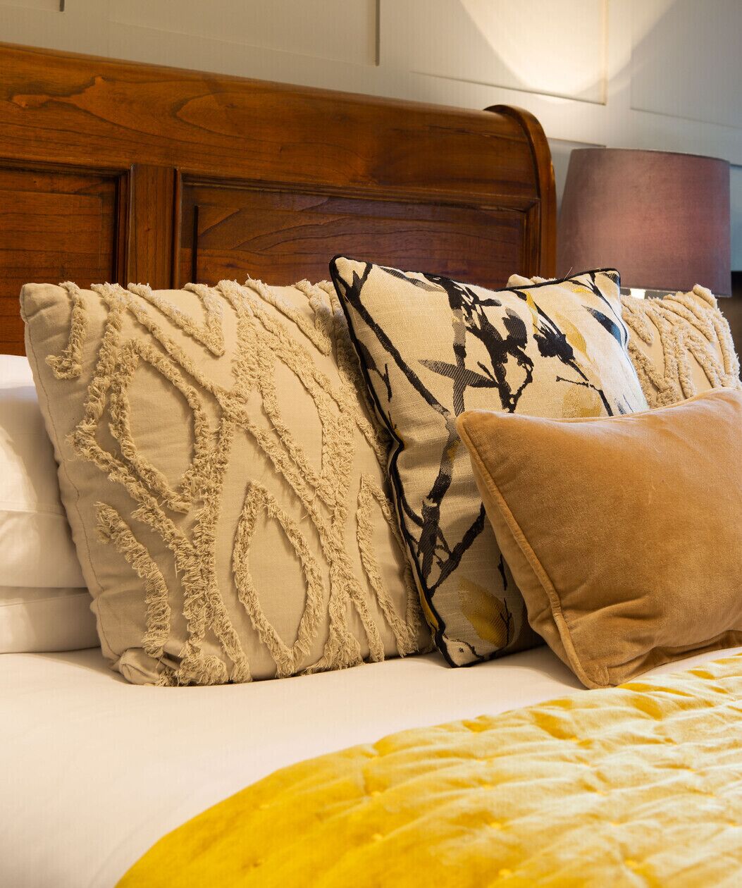 Una cama con cabecera de madera, varias almohadas y una manta amarilla.