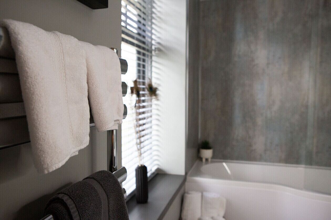 Un baño con toallero, ventana con persianas, lavabo y bañera.