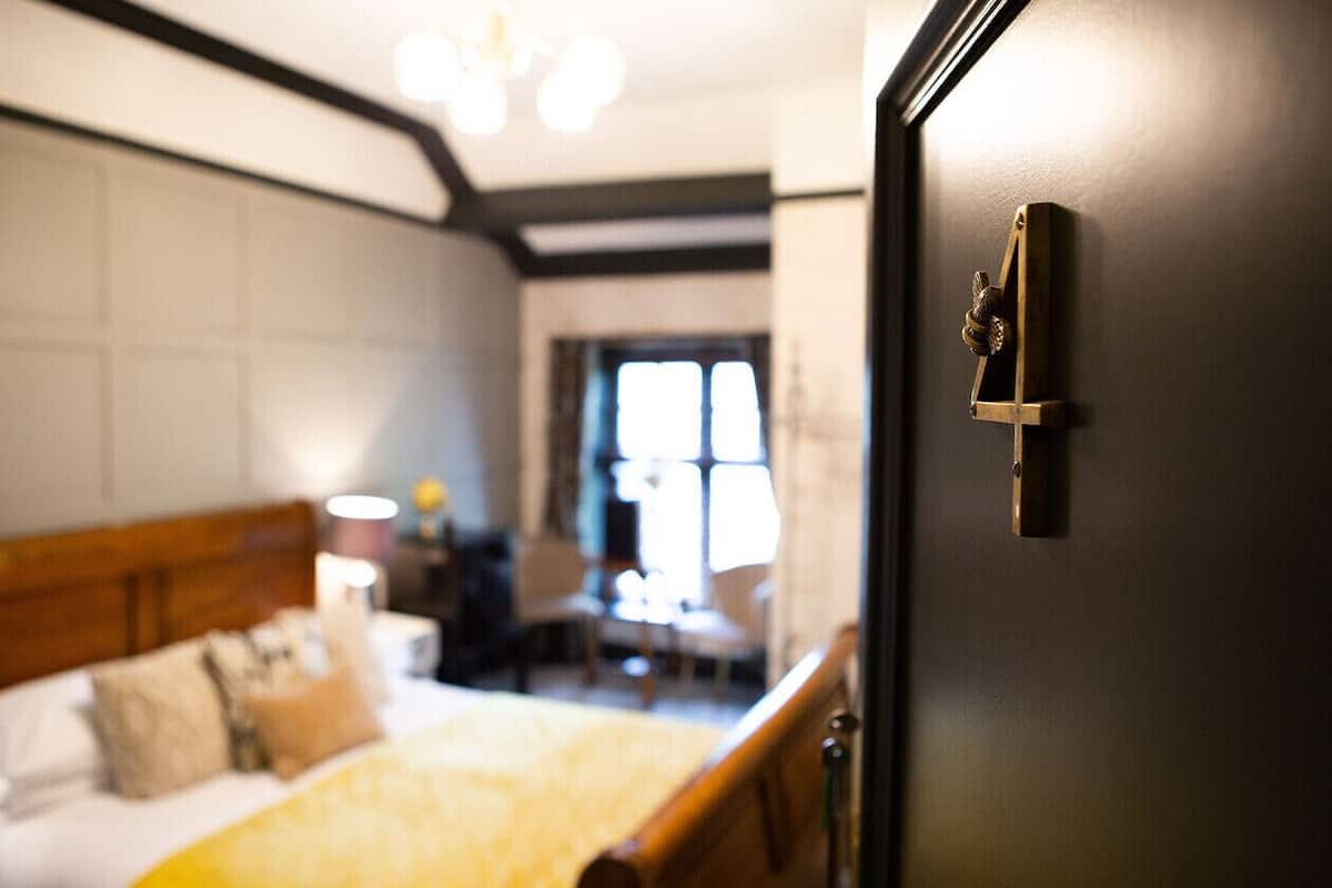 Quarto com cama, mesa de cabeceira e porta com olho de fechadura.