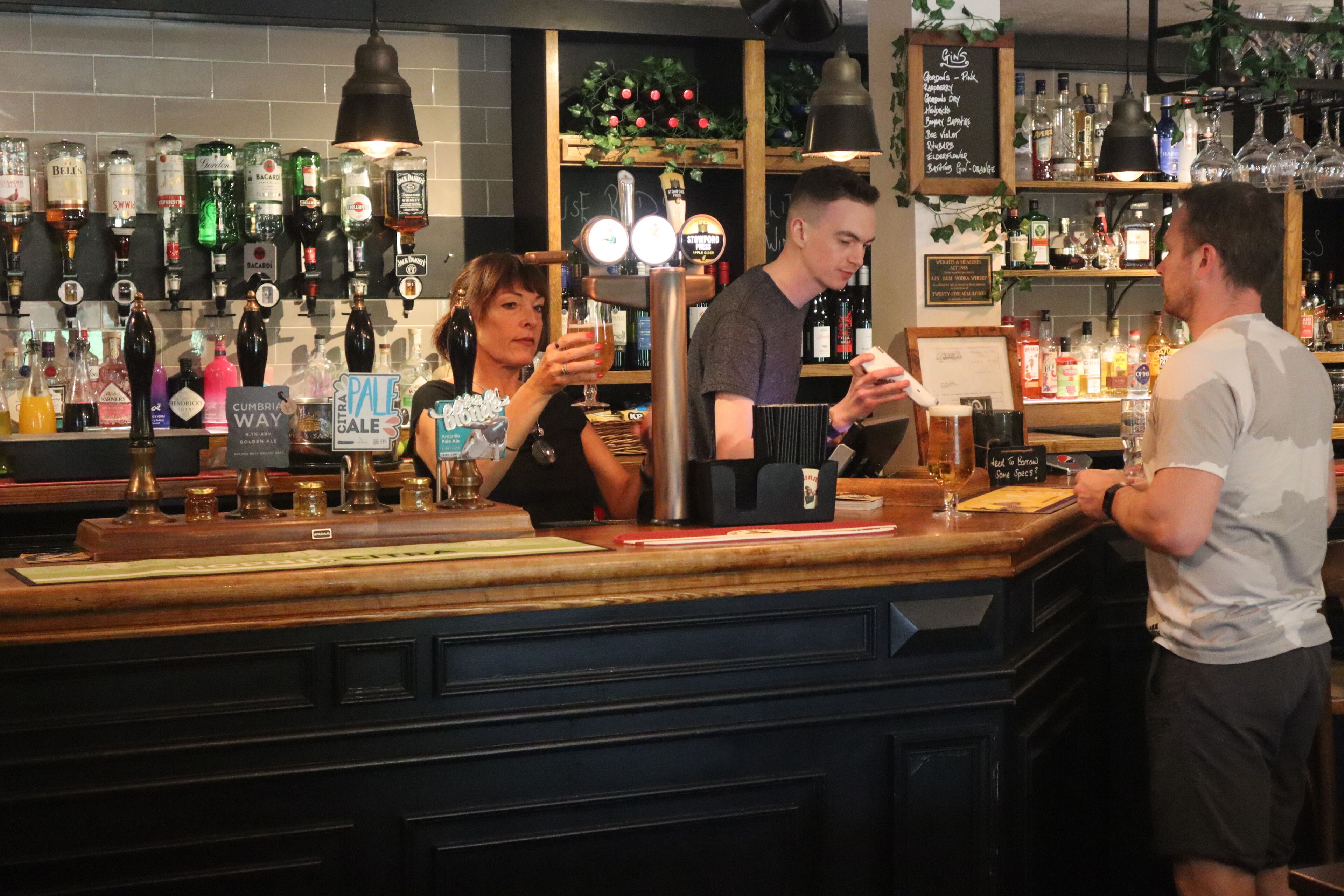 Un bar amb diverses ampolles de licors, una torre de cervesa i un panell amb el menú.