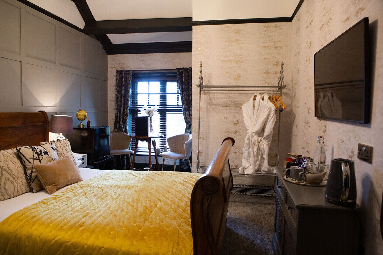 A hotel room with a large bed, a desk with a lamp, a chair, a statue, and a fireplace.