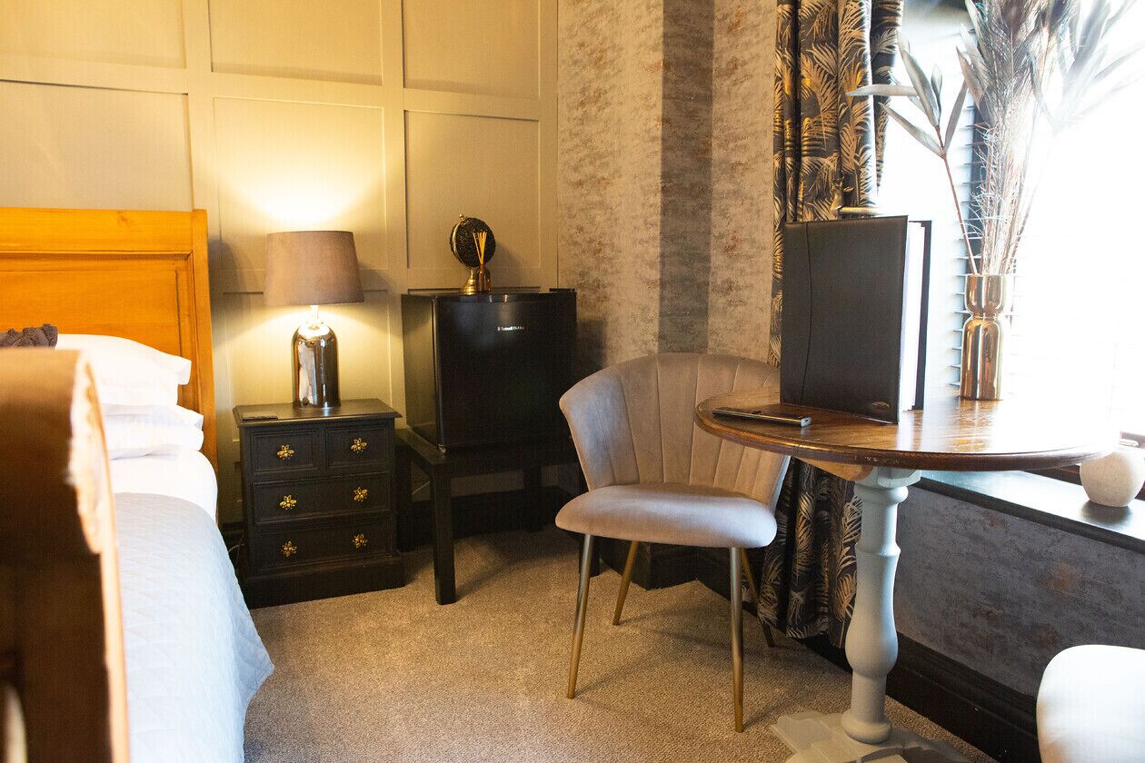 A hotel room with a bed, a desk with a lamp, a chair, a dresser, and a television.