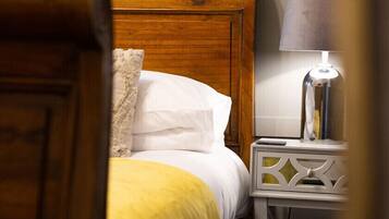 A bed with a wooden headboard, white pillows, and a yellow blanket. There is a bedside table with a lamp and a remote control.