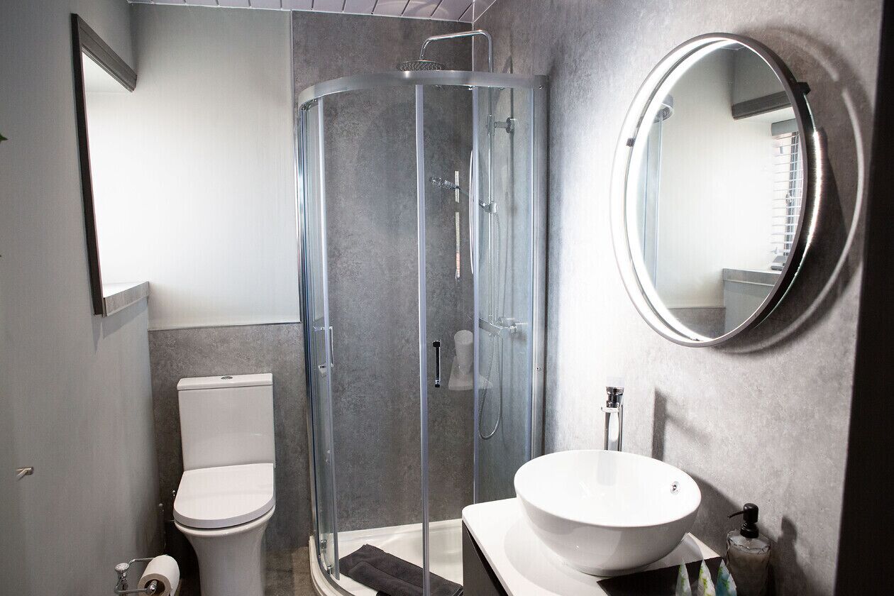 A modern bathroom with a glass-enclosed shower, a white toilet, and a round mirror.