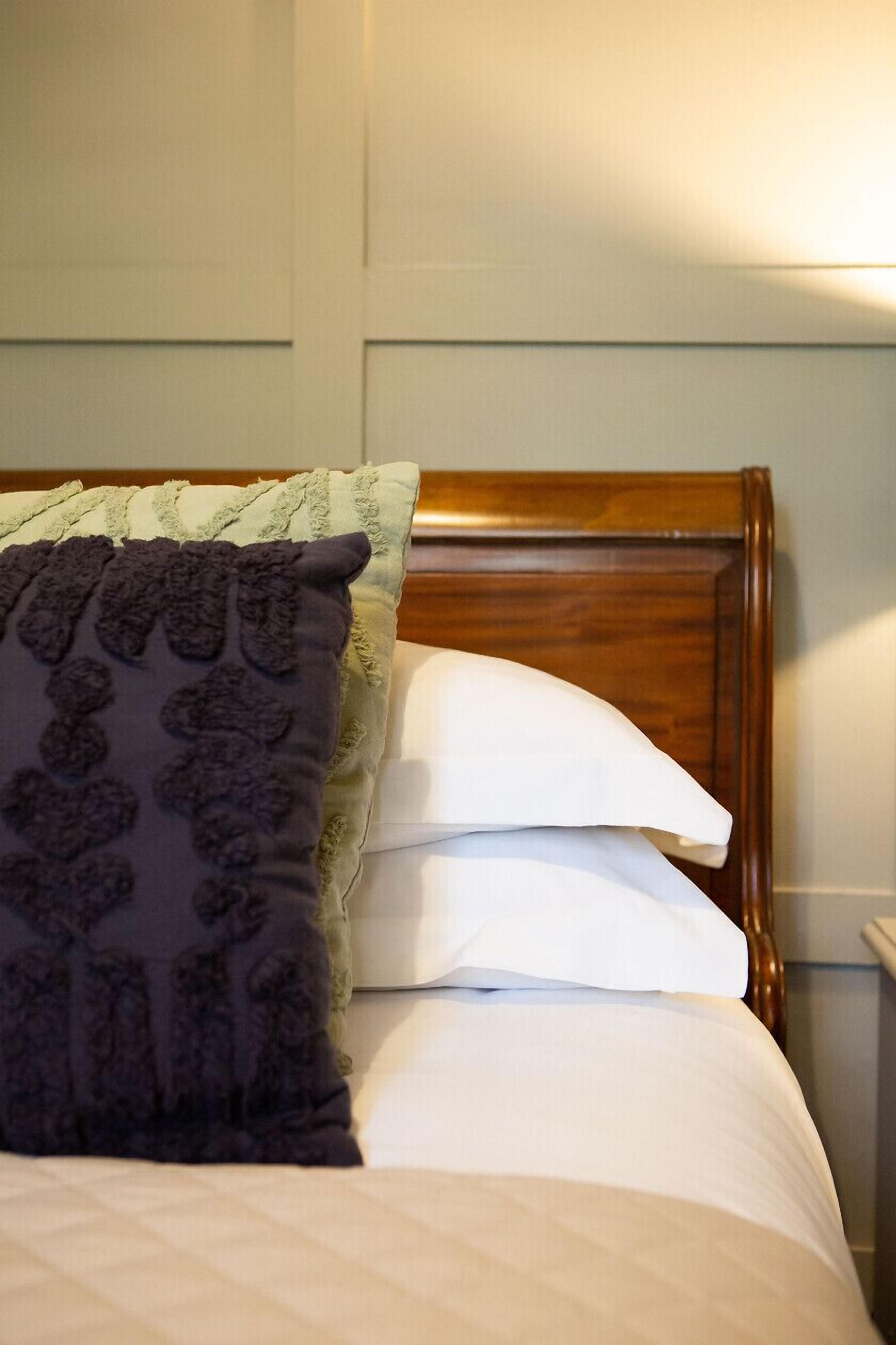 Una cama con cabecera de madera, un almohadón blanco y un almohadón con estampado oscuro.