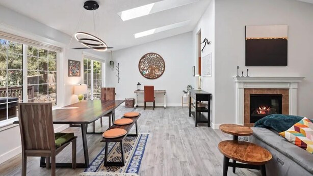 A spacious living room with a wooden dining table, a fireplace, and a large window offering a view of the outdoors.