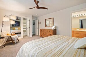 Une chambre à coucher comprenant un lit, une commode, une chaise, un ventilateur de plafond, un placard et une coiffeuse avec un miroir.