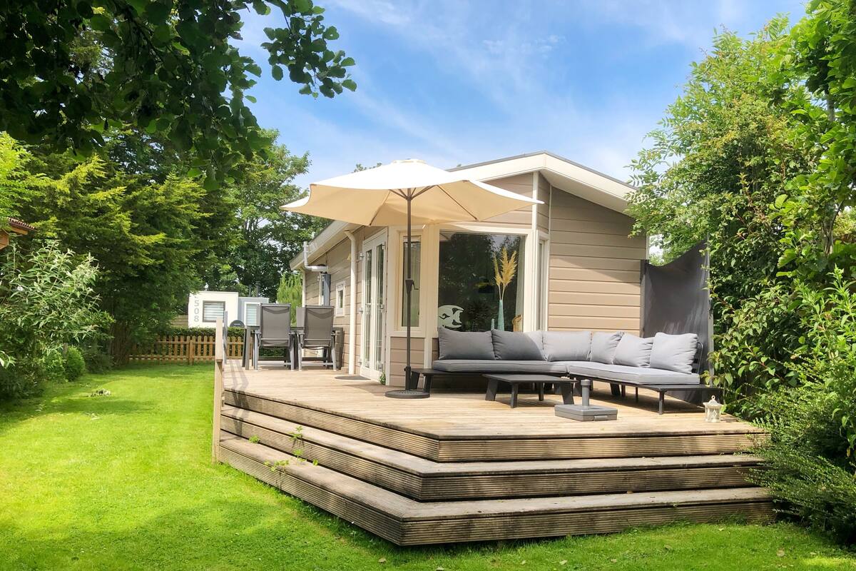 A modern outdoor patio with a built-in sofa and dining area, surrounded by lush greenery.