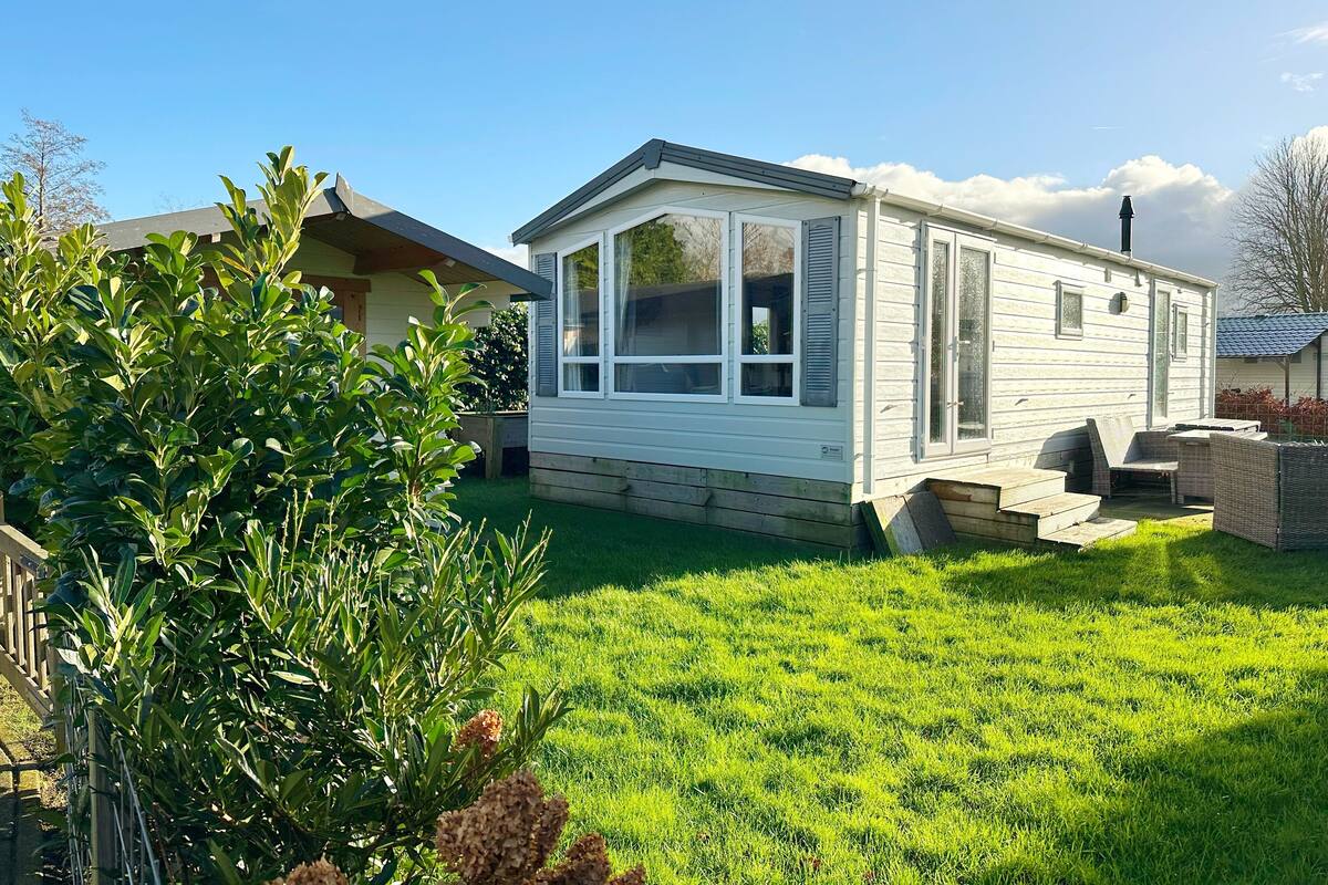 A small, single-story mobile home with a covered porch and a fenced yard.