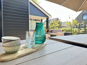 Una mesa de madera con una bandeja que contiene una jarrón de vidrio verde, un vaso transparente y un cuenco estampado.