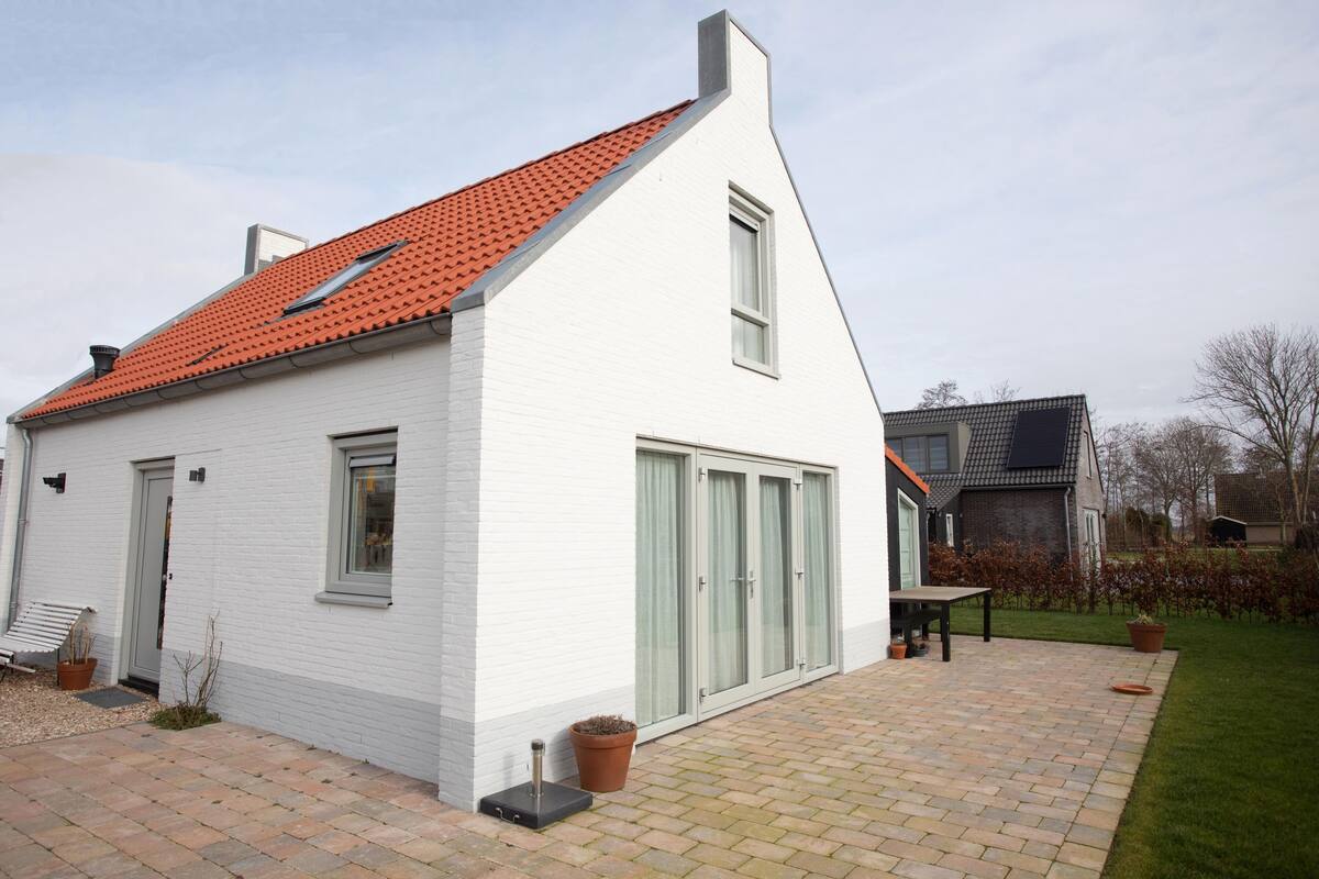 A white house with a red-tiled roof, a patio with a table and chairs, and a small garden area.